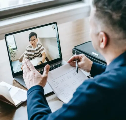 A man wearing a blue suit, in a video call with a another man whose wearing glasses and a striped t shirt